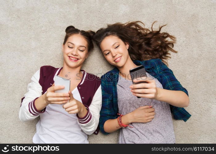 people, friends, teens and friendship concept - happy smiling pretty teenage girls lying on floor with smartphones