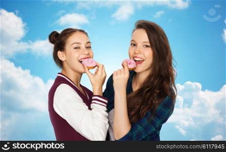 people, friends, teens and friendship concept - happy smiling pretty teenage girls with donuts eating and having fun over blue sky and clouds background
