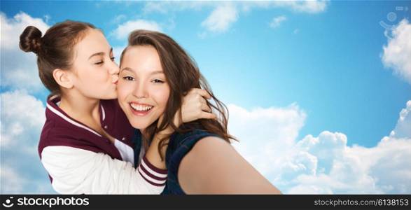 people, friends, teens and friendship concept - happy smiling pretty teenage girls taking selfie and kissing over blue sky and clouds background