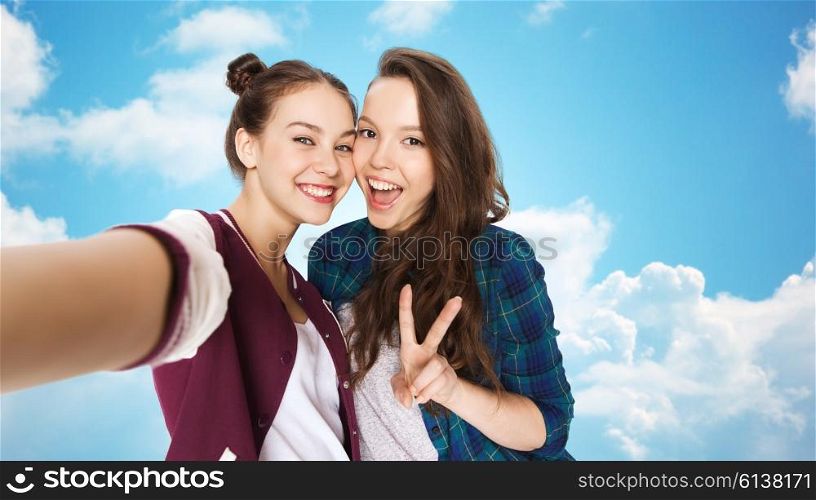 people, friends, teens and friendship concept - happy smiling pretty teenage girls taking selfie and showing peace sign over blue sky and clouds background