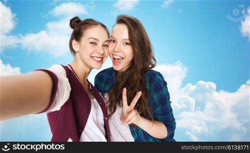 people, friends, teens and friendship concept - happy smiling pretty teenage girls taking selfie and showing peace sign over blue sky and clouds background