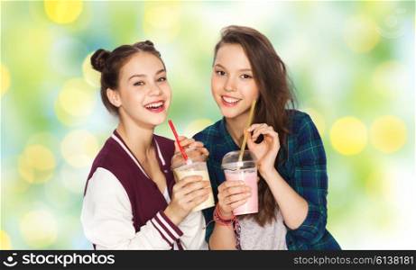 people, friends, teens and friendship concept - happy smiling pretty teenage girls drinking milk shakes and with straw over green holidays lights background