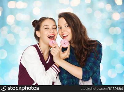 people, friends, teens and friendship concept - happy smiling pretty teenage girls with donuts eating and having fun over blue holidays lights background