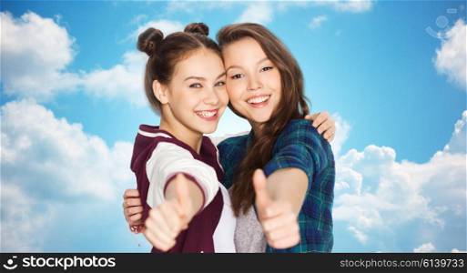people, friends, teens and friendship concept - happy smiling pretty teenage girls hugging and showing thumbs up over blue sky and clouds background
