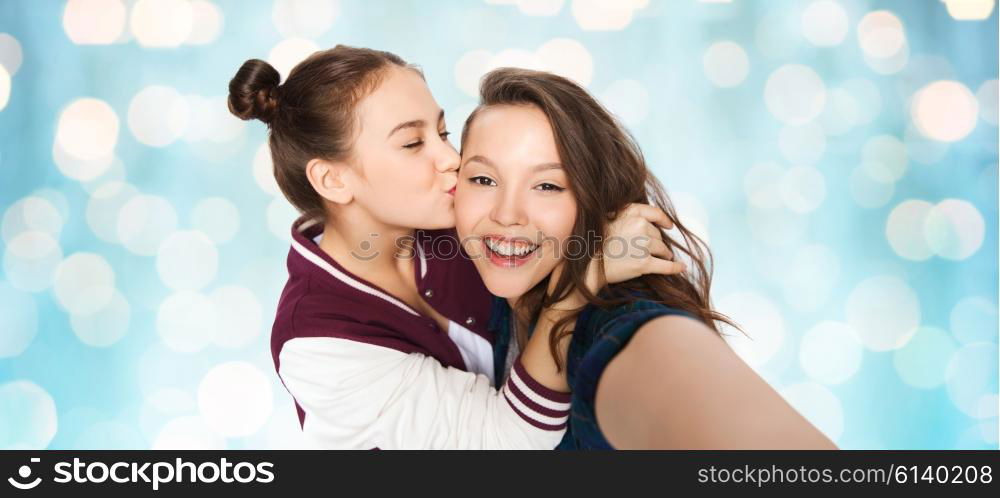 people, friends, teens and friendship concept - happy smiling pretty teenage girls taking selfie and kissing over blue holidays lights background