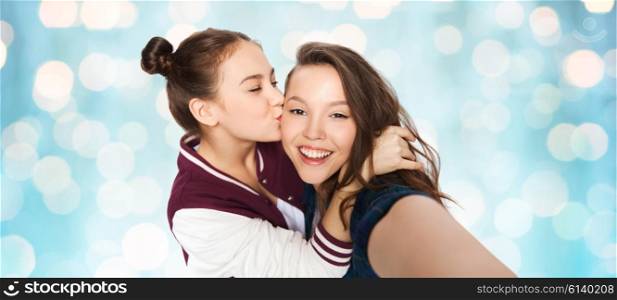 people, friends, teens and friendship concept - happy smiling pretty teenage girls taking selfie and kissing over blue holidays lights background