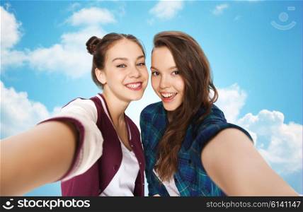 people, friends, teens and friendship concept - happy smiling pretty teenage girls taking selfie over blue sky and clouds background
