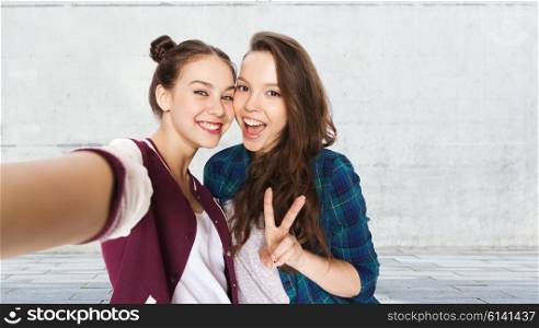 people, friends, teens and friendship concept - happy smiling pretty teenage girls taking selfie and showing peace sign over gray urban street background