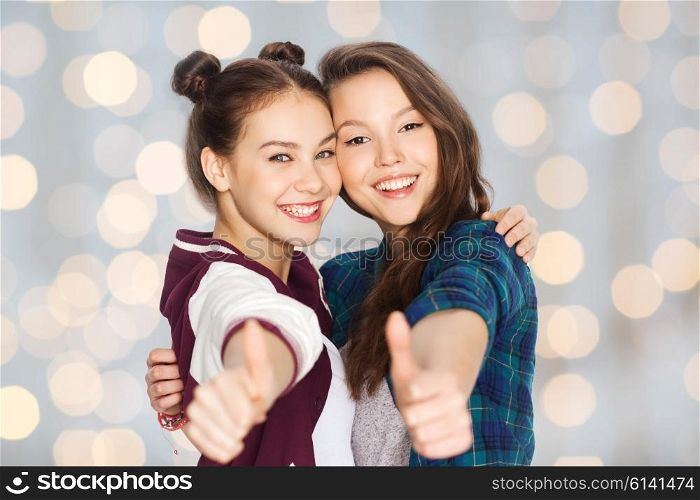 people, friends, teens and friendship concept - happy smiling pretty teenage girls hugging and showing thumbs up over holidays lights background