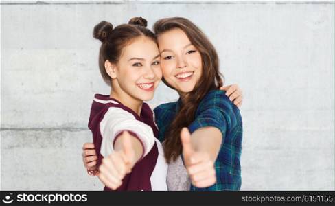 people, friends, teens and friendship concept - happy smiling pretty teenage girls hugging and showing thumbs up over gray stone wall background