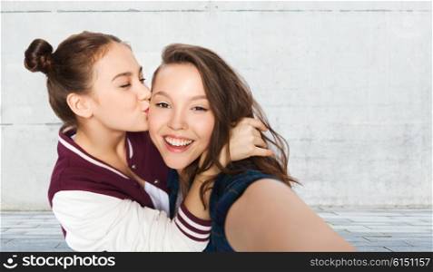 people, friends, teens and friendship concept - happy smiling pretty teenage girls taking selfie and kissing over gray urban street background