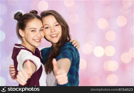 people, friends, teens and friendship concept - happy smiling pretty teenage girls hugging and showing thumbs up over pink holidays lights background