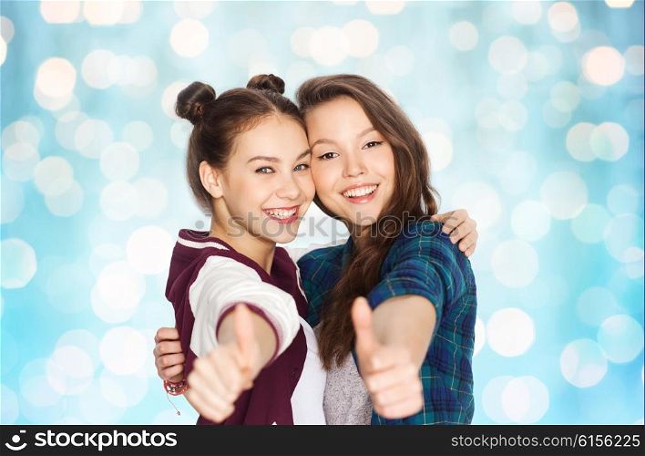 people, friends, teens and friendship concept - happy smiling pretty teenage girls hugging and showing thumbs up over blue holidays lights background