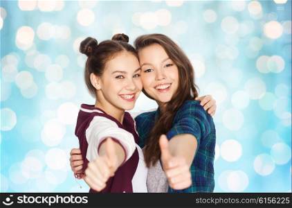 people, friends, teens and friendship concept - happy smiling pretty teenage girls hugging and showing thumbs up over blue holidays lights background
