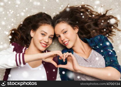 people, friends, winter, christmas and friendship concept - happy smiling pretty teenage girls lying on floor showing heart sign over snow