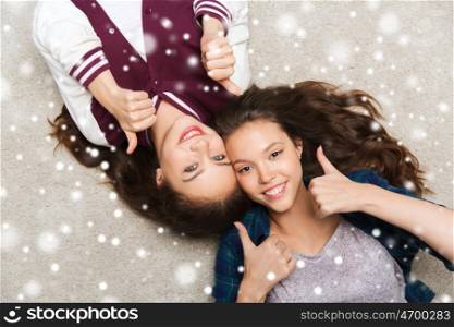 people, friends, winter, christmas and friendship concept - happy smiling pretty teenage girls lying on floor and showing thumbs up over snow