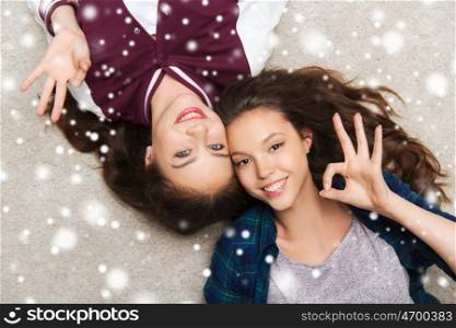 people, friends, winter, christmas and friendship concept - happy smiling pretty teenage girls lying on floor over snow
