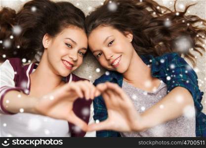 people, friends, winter, christmas and friendship concept - happy smiling pretty teenage girls lying on floor showing heart sign over snow