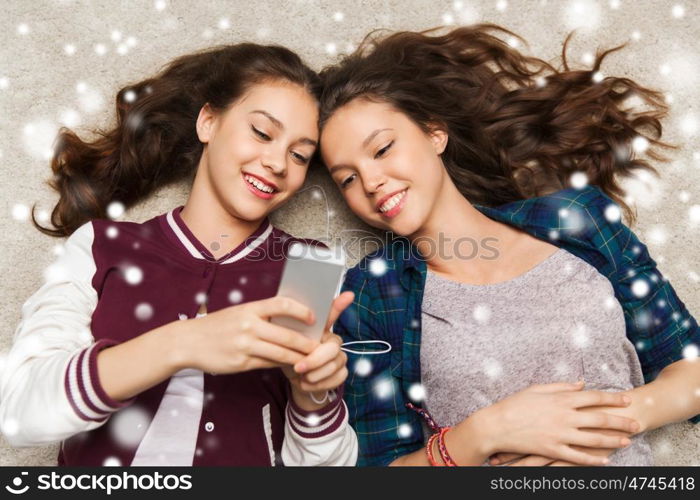 people, friends, winter, christmas and technology concept - happy smiling pretty teenage with smartphones and earphones listening to music over snow