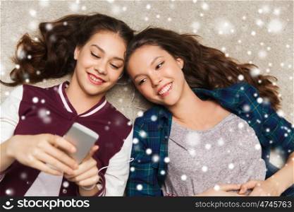 people, friends, winter, christmas and technology concept - happy smiling pretty teenage with smartphones and earphones listening to music over snow