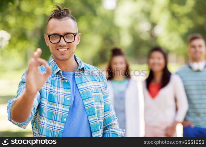 people, friendship and gesture concept - happy smiling man in glasses showing ok hand sign and group of happy friends outdoors. group of happy international friends outdoors. group of happy international friends outdoors