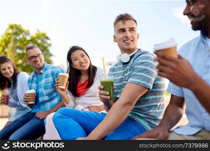 people, friendship and international concept - group of happy friends drinking takeaway coffee and juice talking in city. friends drinking coffee and juice talking in city