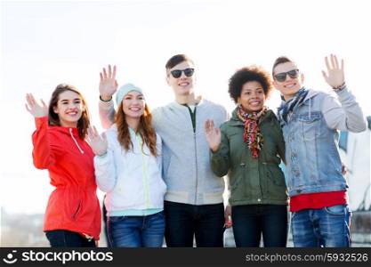 people, friendship and international concept - group of happy teenage friends waving hands on city street