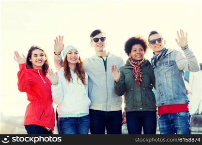 people, friendship and international concept - group of happy teenage friends waving hands on city street