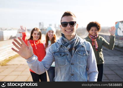 people, friendship and international concept - happy african american young man or teenage boy in front of his friends waving hands on city street