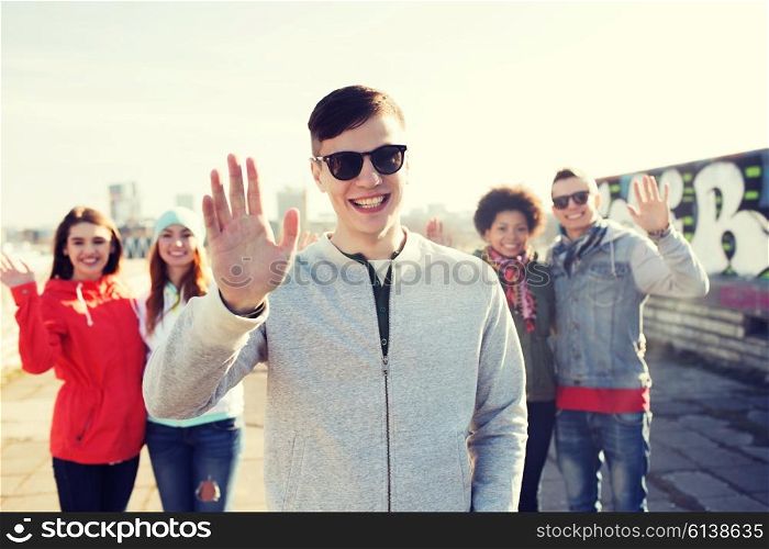 people, friendship and international concept - happy african american young man or teenage boy in front of his friends waving hands on city street