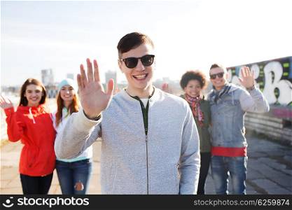 people, friendship and international concept - happy african american young man or teenage boy in front of his friends waving hands on city street