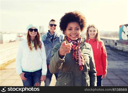 people, friendship and international concept - happy african american young woman or teenage girl pointing finger to you in front of her friends on city street