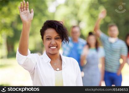 people, friendship and international concept - happy smiling african american woman and group of happy friends waving hands outdoors. group of happy international friends waving hands. group of happy international friends waving hands
