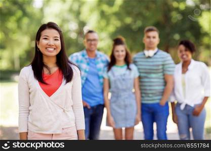 people, friendship and international concept - happy smiling asian woman and group of friends outdoors. group of happy international friends outdoors. group of happy international friends outdoors