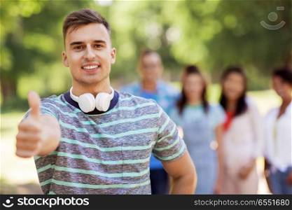 people, friendship and international concept - happy smiling man with headphones showing thumbs up and group of happy friends outdoors. group of happy international friends outdoors. group of happy international friends outdoors