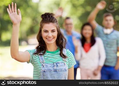 people, friendship and international concept - happy smiling woman and group of happy friends waving hands outdoors. group of happy international friends waving hands. group of happy international friends waving hands