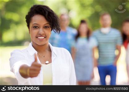 people, friendship and international concept - happy smiling woman showing thumbs up and group of happy friends outdoors. group of happy international friends outdoors. group of happy international friends outdoors