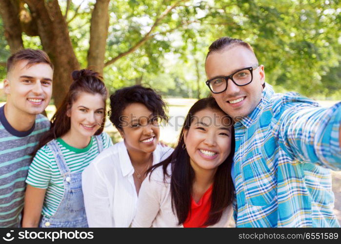 people, friendship and international concept - happy smiling young woman and group of happy friends taking selfie outdoors. group of happy international friends taking selfie. group of happy international friends taking selfie