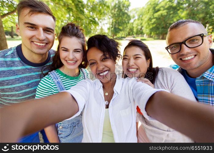 people, friendship and international concept - happy smiling young woman and group of happy friends taking selfie outdoors. group of happy international friends taking selfie. group of happy international friends taking selfie