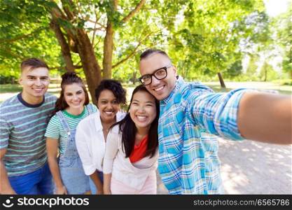 people, friendship and international concept - happy smiling young woman and group of happy friends taking selfie outdoors. group of happy international friends taking selfie