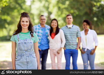 people, friendship and international concept - happy smiling young woman and group of happy friends outdoors. group of happy international friends outdoors. group of happy international friends outdoors