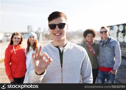 people, friendship and international concept - happy young man or teenage boy in front of his friends showing ok sign on city street