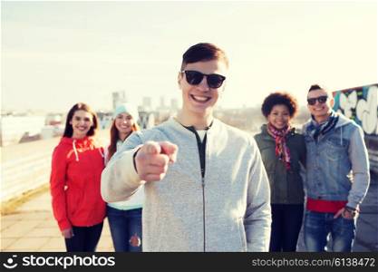 people, friendship and international concept - happy young man or teenage boy pointing finger to you in front of his friends on city street