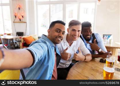 people, friendship and leisure concept - happy male friends drinking beer, taking selfie and showing thumbs up at bar or pub. friends taking selfie and drinking beer at bar