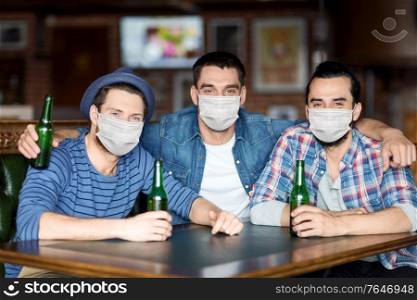 people, friendship and pandemic concept concept - male friends in face protective medical mask for protection from virus disease drinking bottled beer and hugging at bar or pub. male friends in masks drinking beer at bar or pub