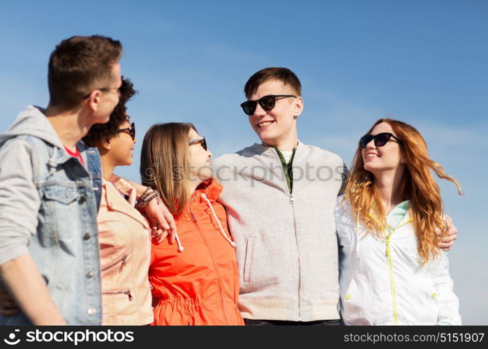 people, friendship and teenage concept - group of happy friends in sunglasses hugging and talking on city street. happy teenage friends in shades talking on street