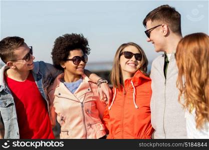 people, friendship and teenage concept - group of happy friends in sunglasses hugging and talking on city street. happy teenage friends in shades talking on street