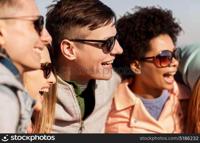 people, friendship and teenage concept - group of happy friends in sunglasses having fun and laughing outdoors. happy teenage friends in shades laughing outdoors