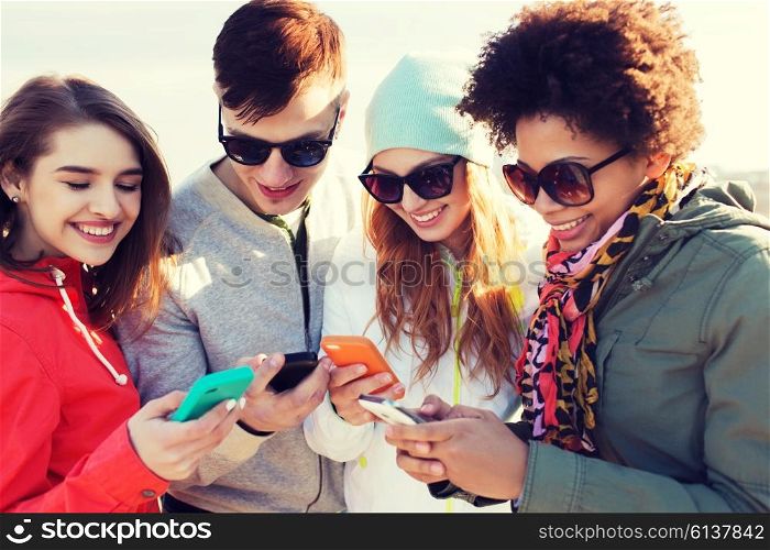 people, friendship, cloud computing and technology concept - group of smiling teenage friends with smartphone outdoors