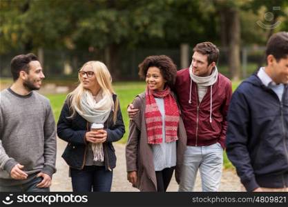 people, friendship, communication and international concept - group of happy friends walking along autumn park and drinking coffee